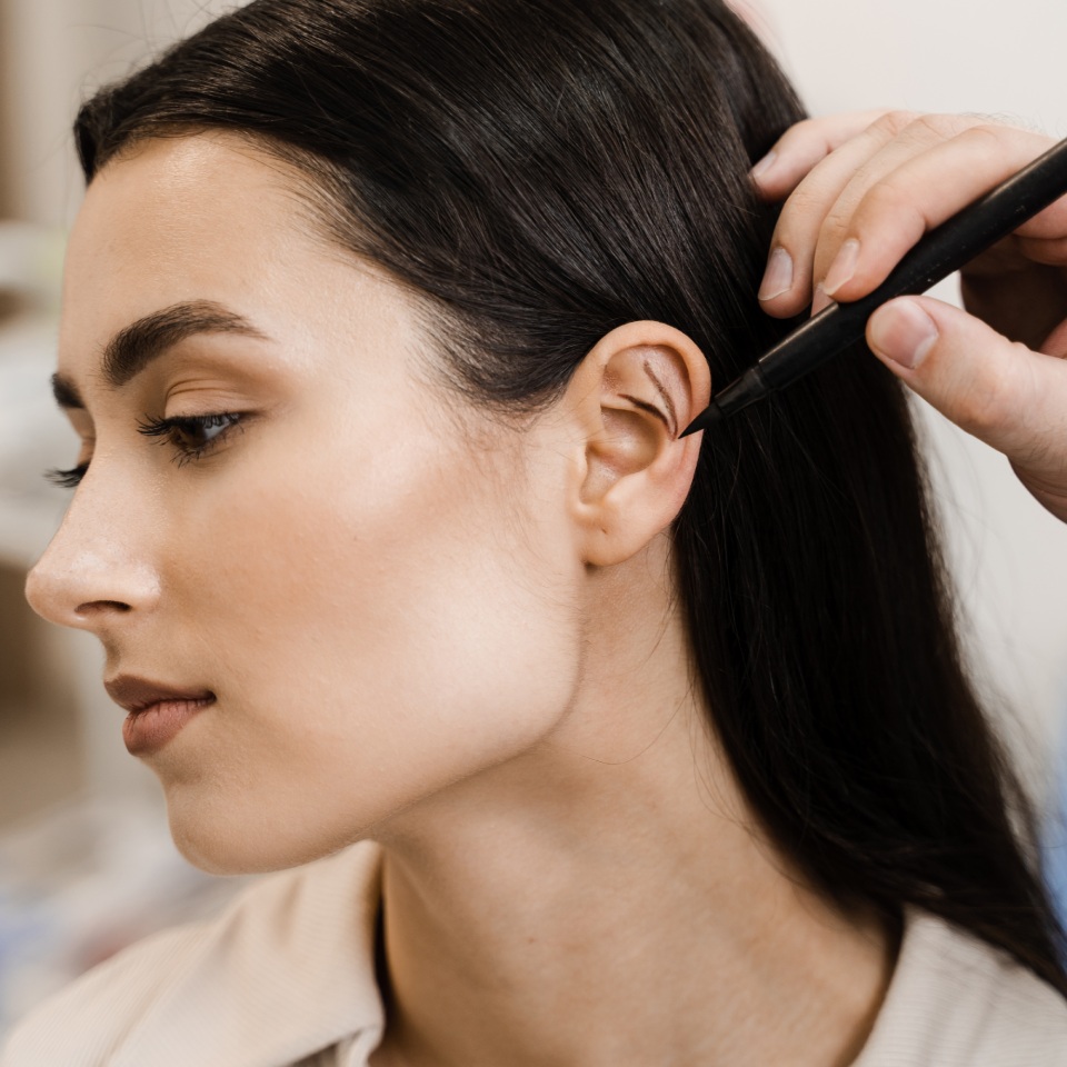 A person drawing on a woman's ear with a pen.