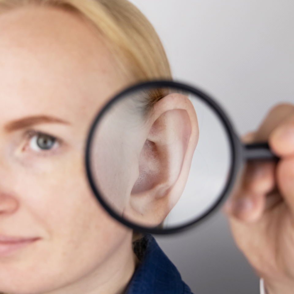 A person holds a magnifying glass up to their ear, enlarging its appearance.