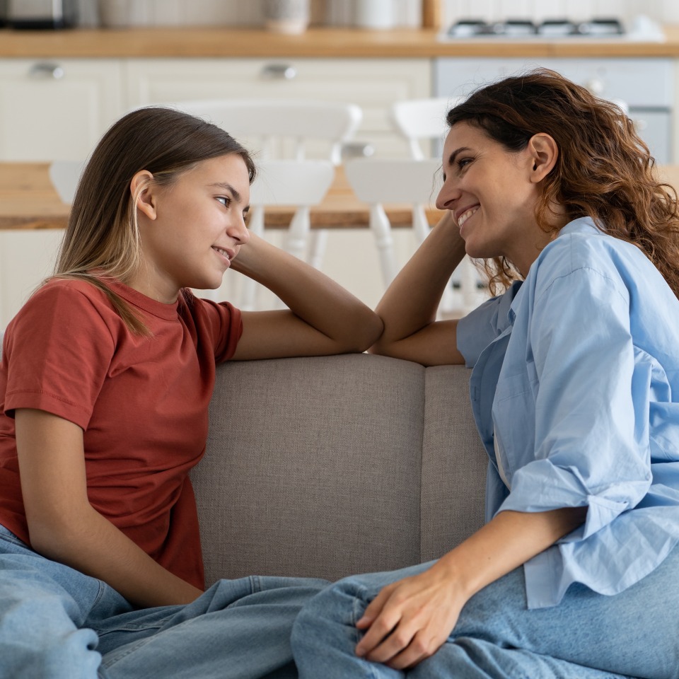 Two people sitting on a couch, smiling at each other in a cozy living room.