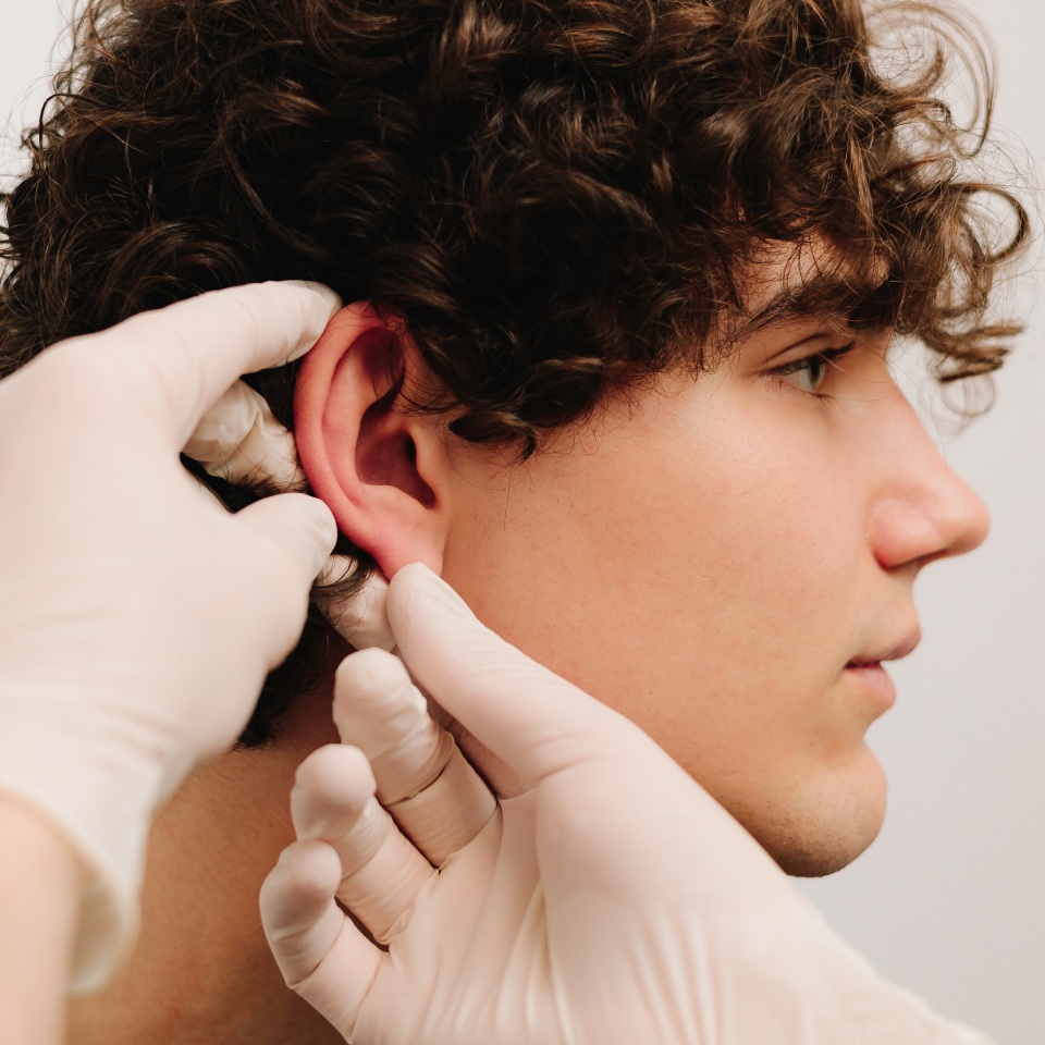 A person with curly hair is having an ear exam performed by someone wearing white gloves.