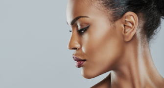 Profile view of a woman with tied-back hair and a neutral expression against a gray background.